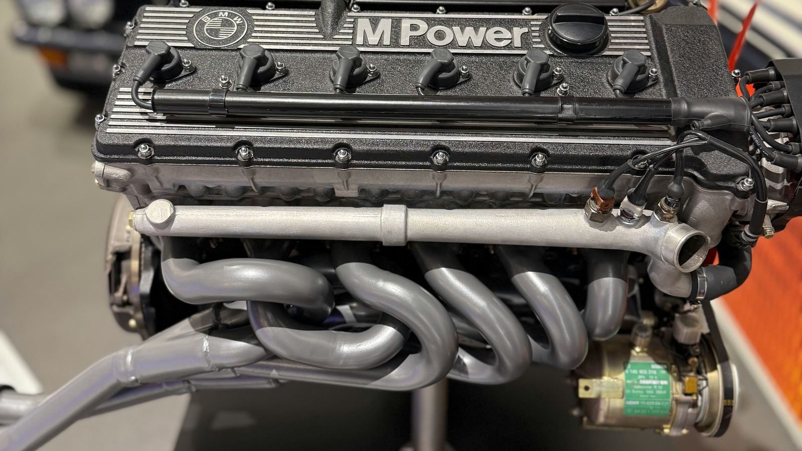 Classic BMW M Power straight-six engine with tubular exhaust manifold on a display stand