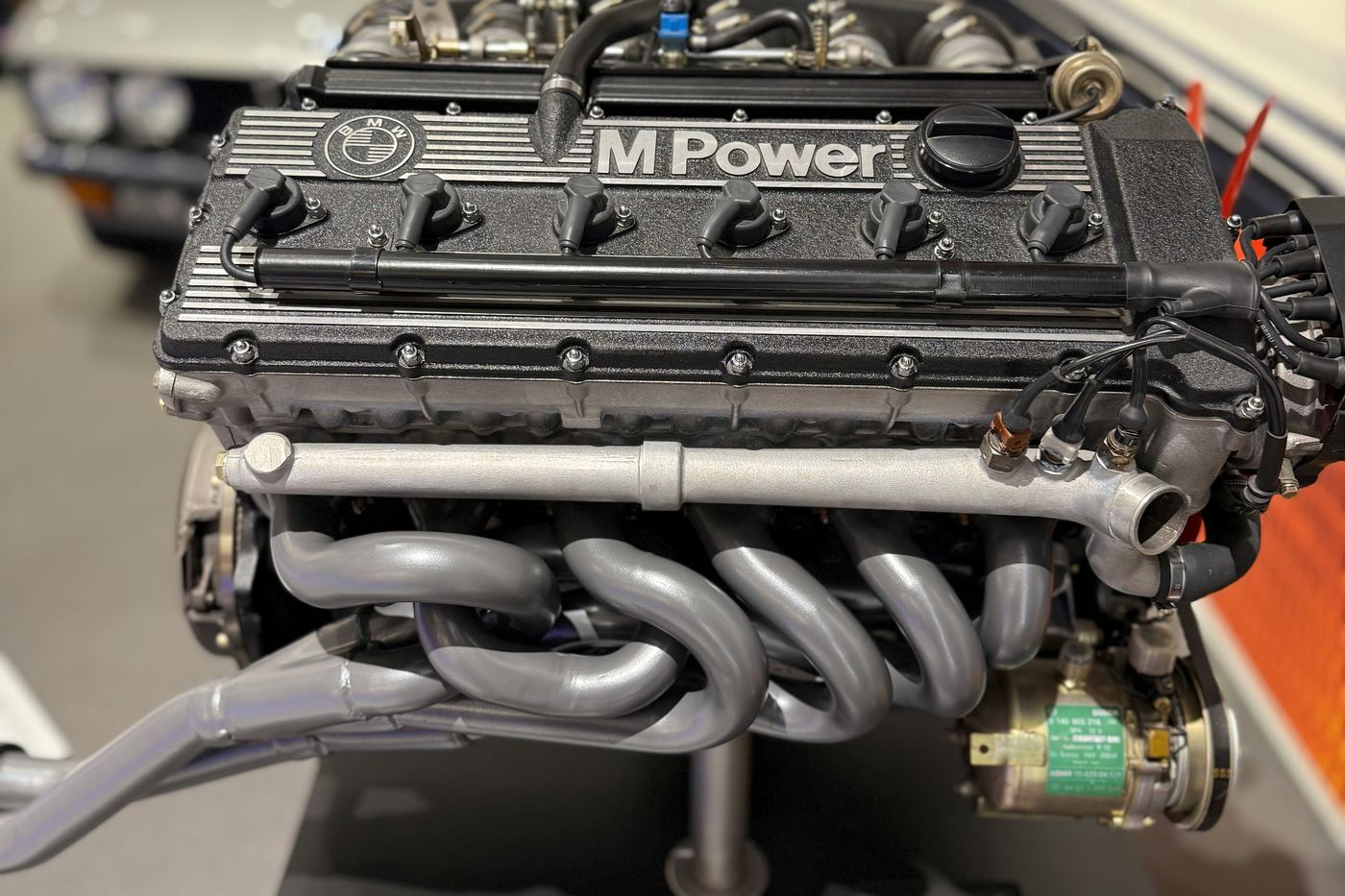 Classic BMW M Power straight-six engine with tubular exhaust manifold on a museum display stand